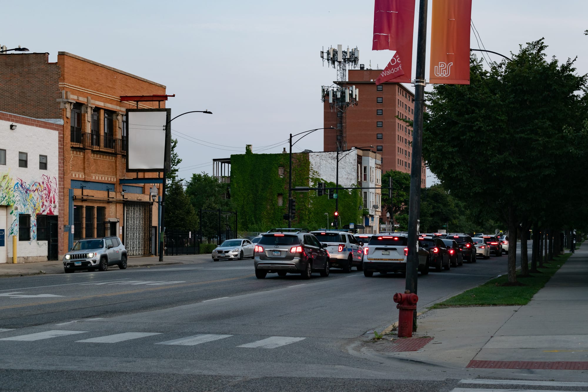 cars stopped at a traffic light, red fire hydrant, ivy-covered brick building, cell phone tower